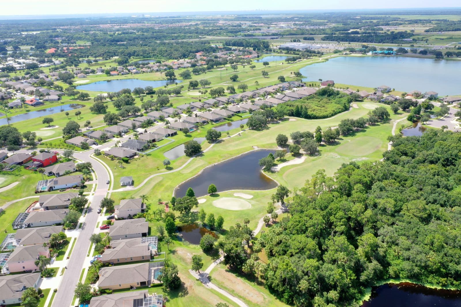 Aerial view of a suburban neighborhood with a golf course, several lakes, and green forests.