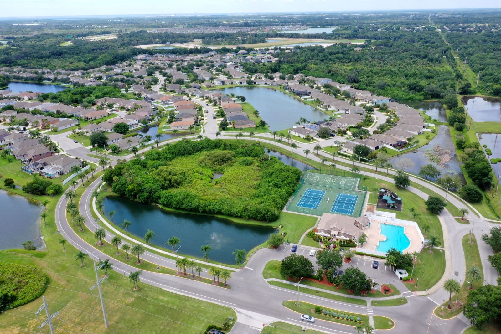 Aerial view of a suburban neighborhood with houses, ponds, tennis courts, and a community pool.